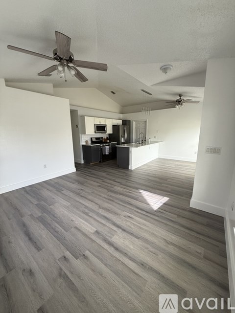 A room with a ceiling fan and a kitchen in the background.