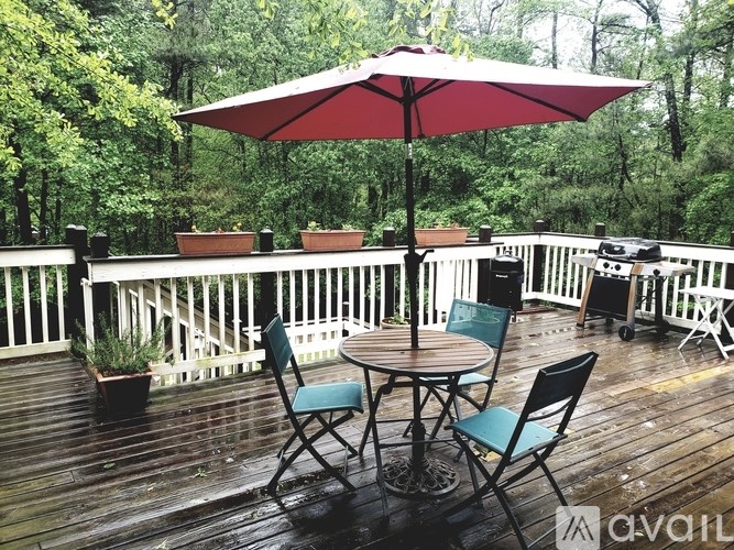 A red umbrella is on a wooden deck with a table and chairs.