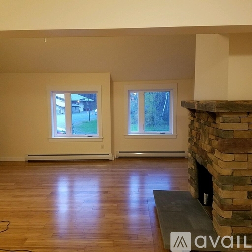 A living room with a stone fireplace and two windows.