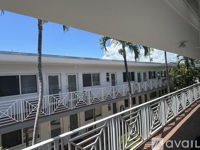 A white building with balconies and palm trees in the background.