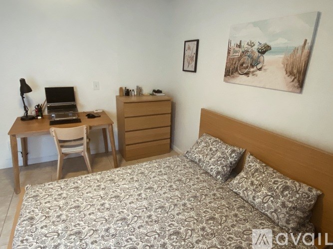 A bedroom with a bed, desk, chair, and a painting on the wall.