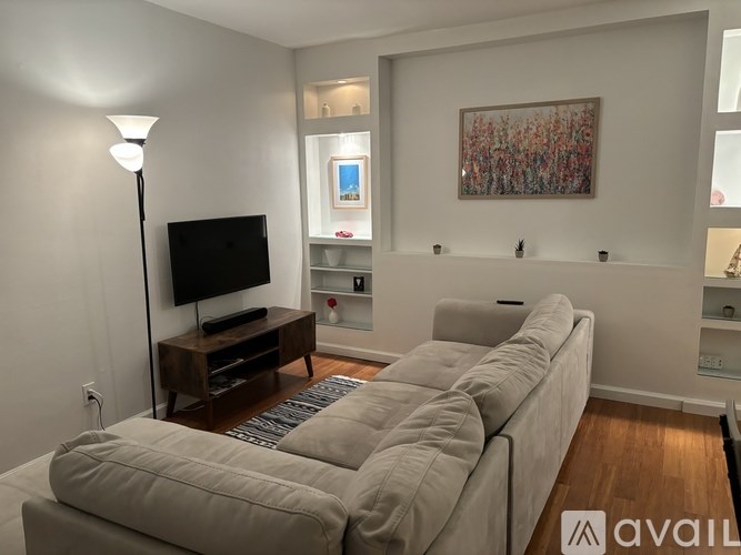 A living room with a grey couch, a television, and a painting on the wall.