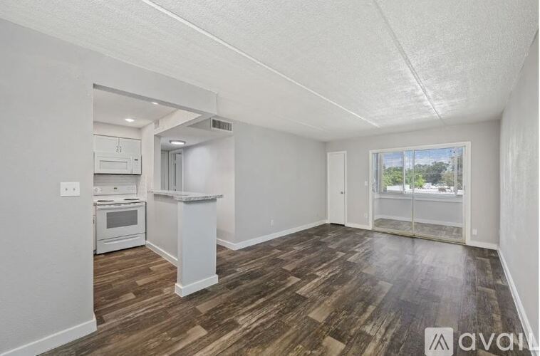 A room with wooden flooring and white walls, featuring a kitchen area with a refrigerator, oven, and microwave.