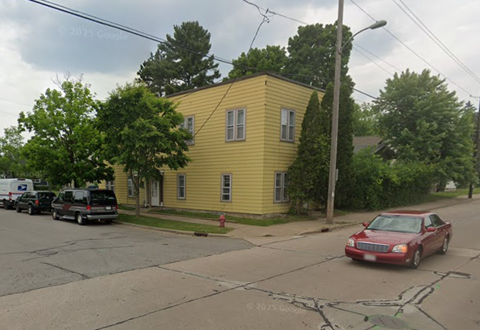 A yellow house with a red car parked in front.
