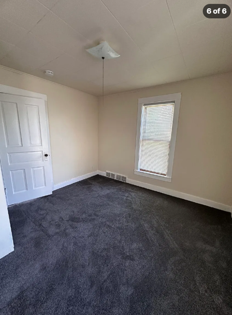 A room with a carpeted floor, a window with blinds, and a white door.
