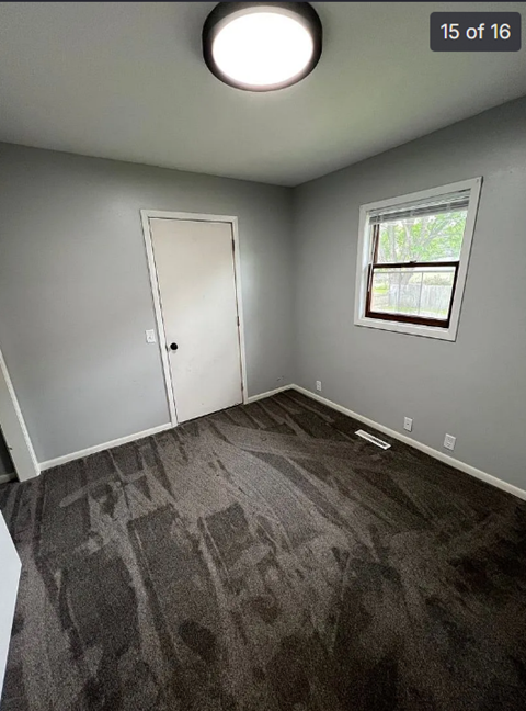 A room with grey carpet and a window.