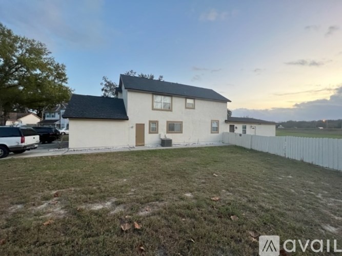 A house with a white exterior and a black roof is surrounded by a white fence.
