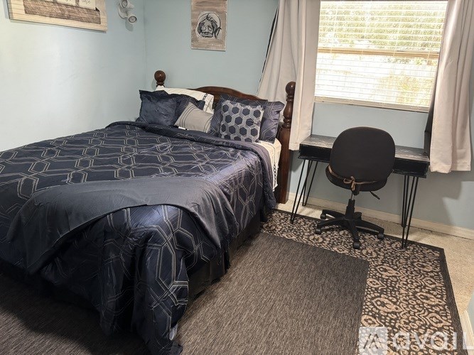 A bed with a blue comforter and a chair with a black seat and back.