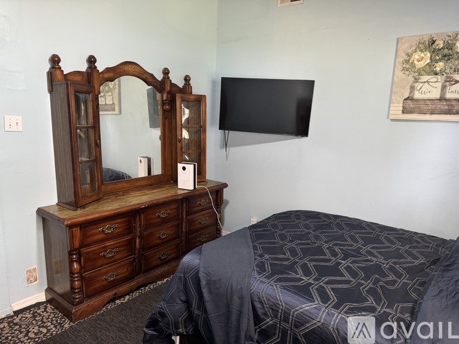 A bedroom with a bed, a wooden dresser, and a TV mounted on the wall.