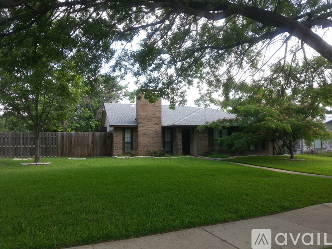 A house with a brick chimney is surrounded by a green lawn and trees.