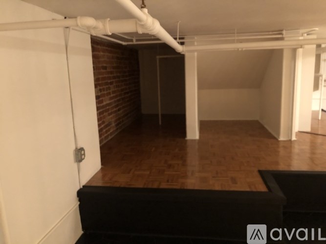 A room with a wooden floor and a white ceiling with a pipe running across it.