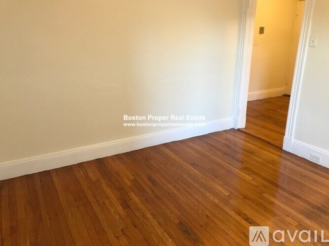 A room with wooden flooring and white walls, with a website address for Boston Proper Real Estate.