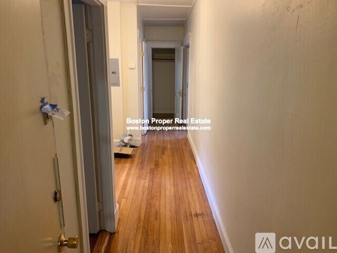 A hallway with wooden floors and white walls, leading to a door at the end.