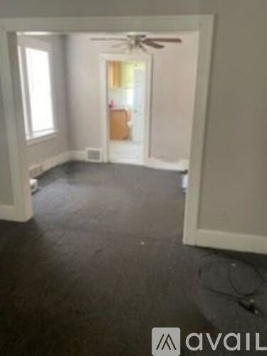 A room with a fan and a doorway leading to another room.