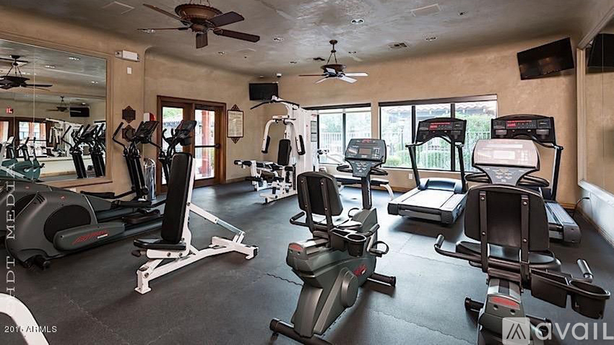 A spacious home gym with various exercise equipment and a ceiling fan.
