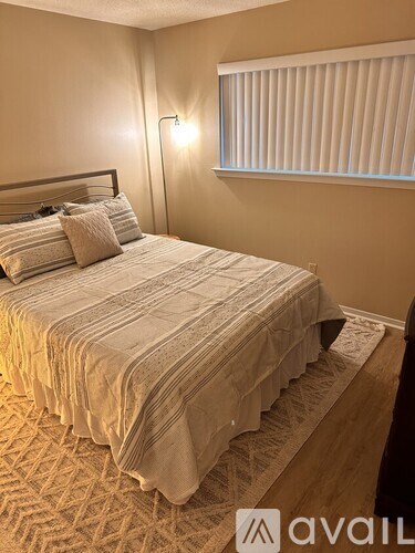 A bed with a striped comforter and pillows in a room with a window covered by blinds.