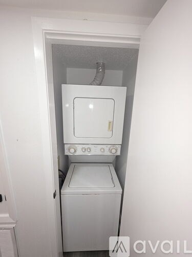 A small white laundry machine sits in a narrow space.