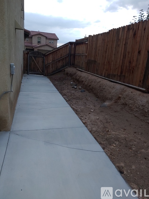 A concrete pathway leads to a house with a wooden fence on the right.