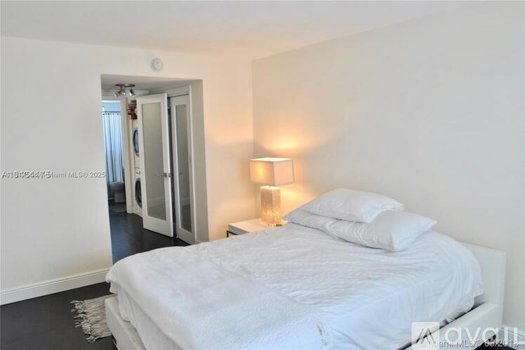 A bedroom with a white bed and a lamp on the side table.
