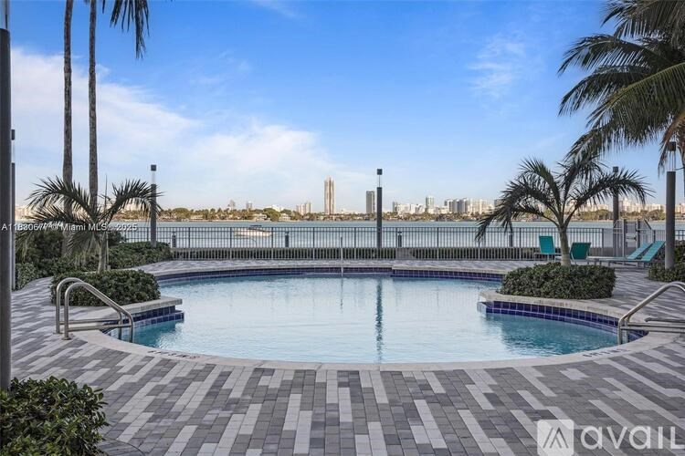 A large outdoor swimming pool surrounded by palm trees and a city skyline in the distance.