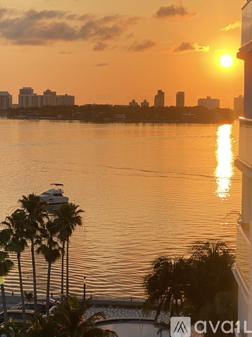 A sunset view from a balcony overlooking a body of water with palm trees and buildings in the distance.