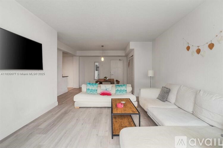 A living room with a white couch, a coffee table, and a television on the wall.