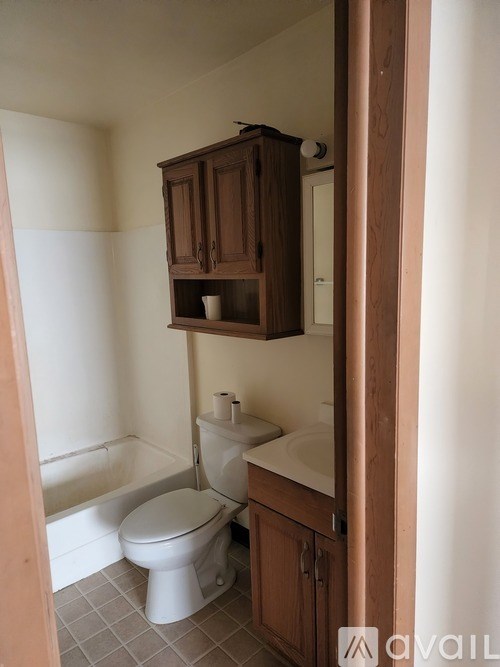A small bathroom with a toilet, sink and wooden cabinet.