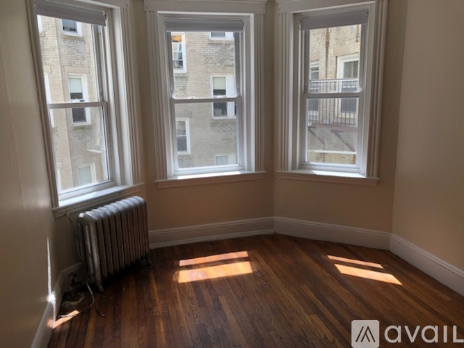 A room with wooden floors and three windows showing an outside view.
