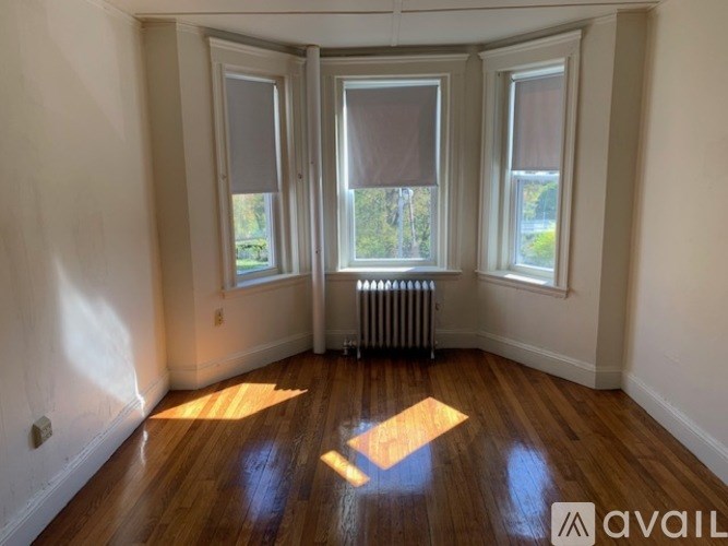 A room with wooden floors and three windows with blinds.