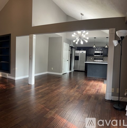 A large open space with wood flooring and a kitchen area in the background.