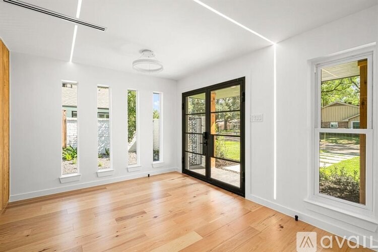 A room with wooden floors and white walls, with a view of a street through a window.
