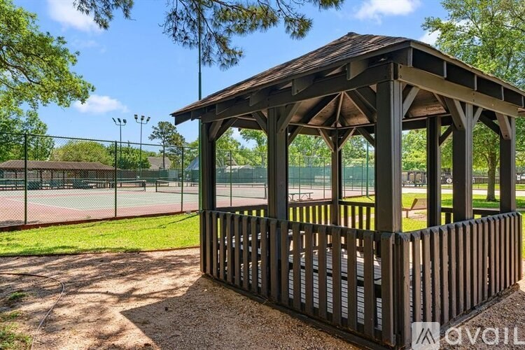 A gazebo is located in a park with a tennis court in the background.