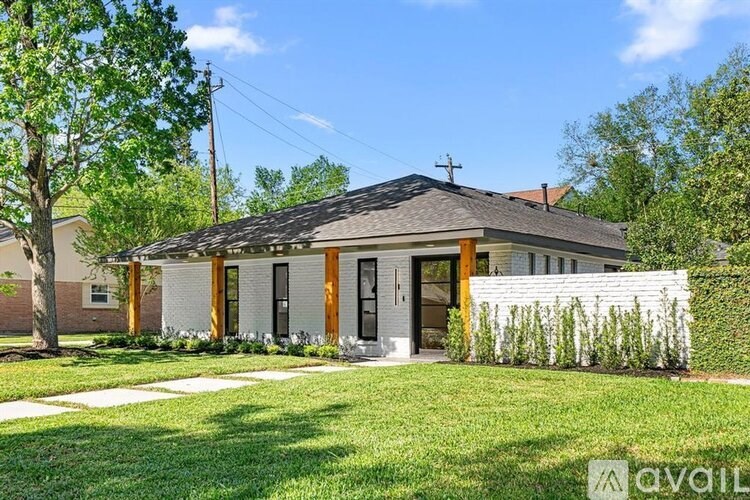 A house with a brown roof and a white wall is surrounded by greenery.
