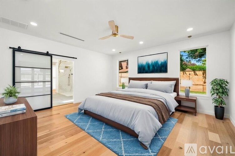 A bedroom with a bed, a ceiling fan, and a window with a view of a forest.