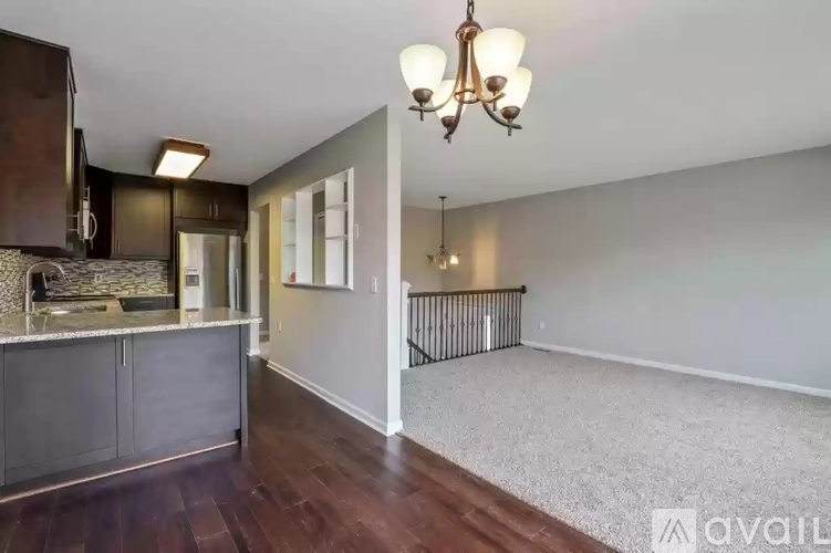 A well-lit room with a chandelier, a kitchen area, and a carpeted floor.