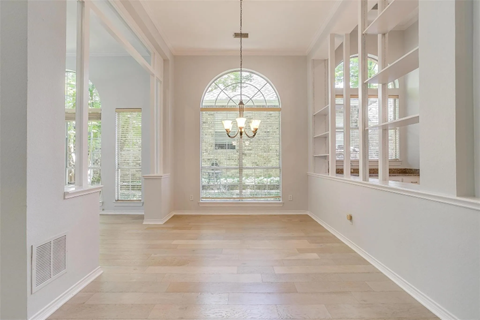 A spacious room with a large arched window and a chandelier hanging from the ceiling.