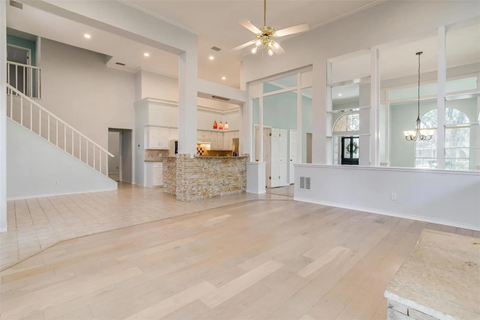 A spacious room with wooden floors and a staircase on the left side.