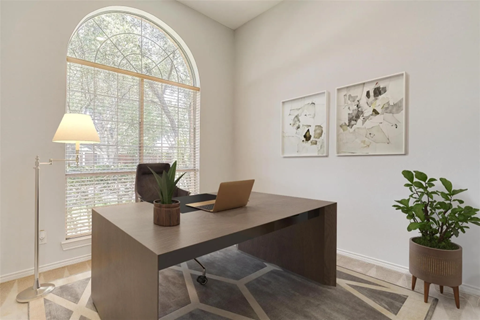 A room with a desk, chair, and two potted plants.