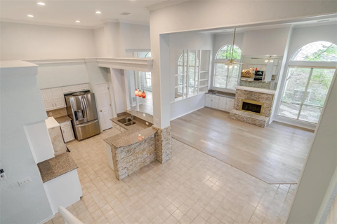 A spacious living room with a stone fireplace and a kitchen area with white cabinets.
