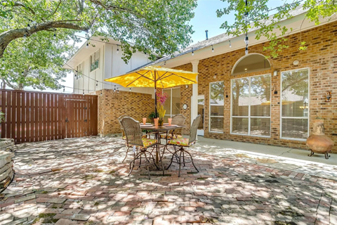 A patio with a table and chairs under a yellow umbrella.