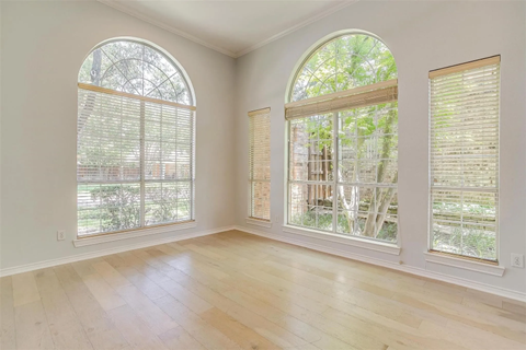A room with wooden floors and three windows with blinds.