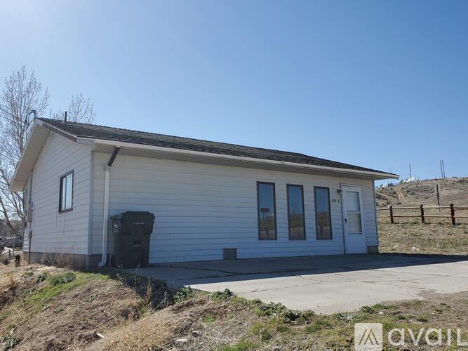 A small white building with a black door and windows is situated on a hill.