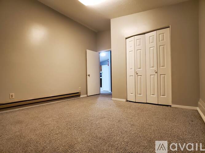 A room with a carpeted floor, a white door, and a white wall.
