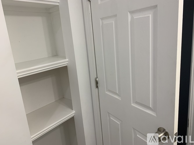A white door is open to a white pantry with empty shelves.