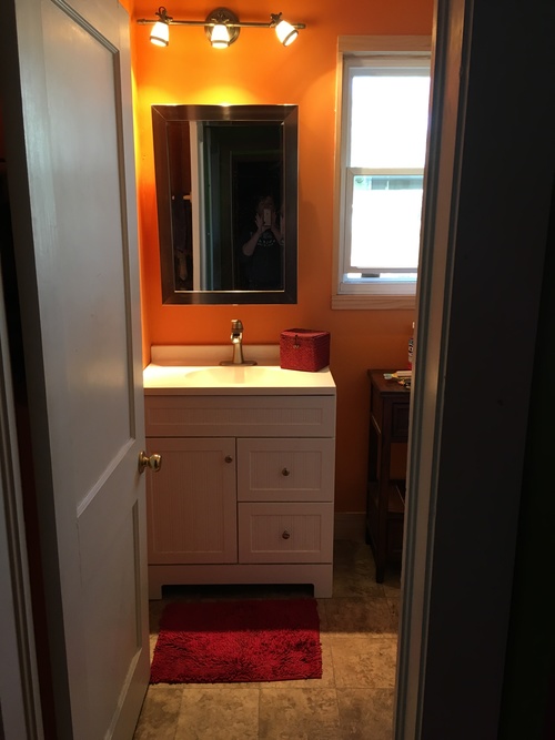 A bathroom with a sink, mirror and red rug.