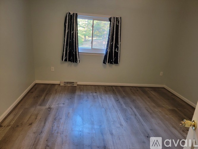 A room with wooden flooring and a window with curtains.