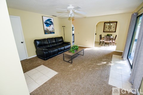 A living room with a black leather couch and a ceiling fan.
