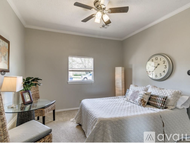 A bedroom with a bed, a table, a chair, a fan, a clock, and a window.