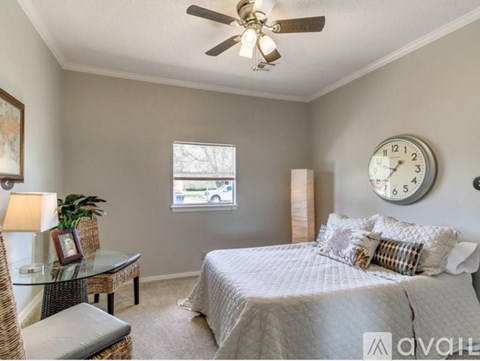 A bedroom with a bed, a table, a chair, a fan, a clock, and a window.