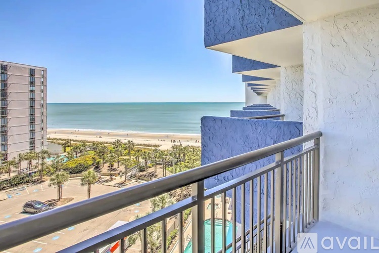 A balcony overlooks a beach with a building and palm trees in the distance.